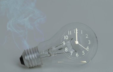 Çalışan bir kurum ve siyah bir analog saat içeren bir ampul soyutlayın. Gezegendeki kaynakların korunması, elektrik tüketiminin gelecek nesiller için azaltılması kavramını göster.