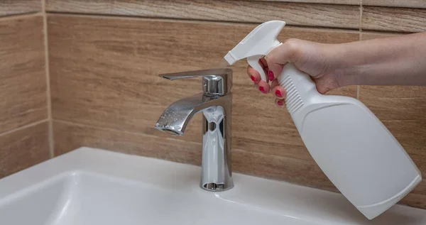 Cleaning the tap with detergent in the bathroom. A woman's hand sprays detergent on the tap. Bathroom cleaning. Place for text on bottle from detergents.