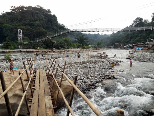 Bukit Lawang, Endonezya, 17 Ocak 2018: Endonezya 'nın Kuzey Sumatra eyaletindeki Bukit Lawang' da Bahorok Nehri 'ni geçen ahşap bir köprünün yanında yıkanan insanlar.