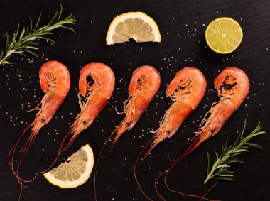 Siyah taş tabakta limonlu karides, limon ve rosmary. Üst görünüm.