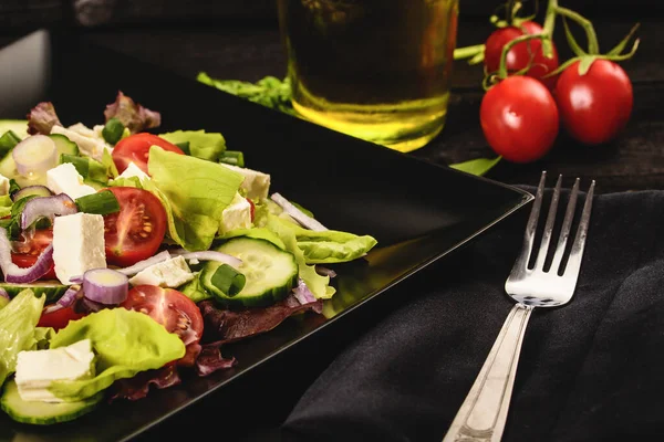 Domates, salatalık, marul, kırmızı soğan ve siyah tabakta peynirli taze Yunan salatası.