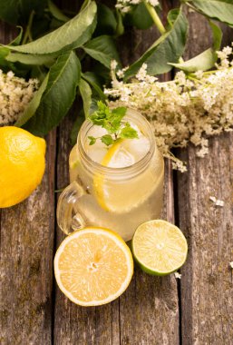 Ev yapımı Elderflower limonata, limon dilimi ve ahşap arka planda nane..