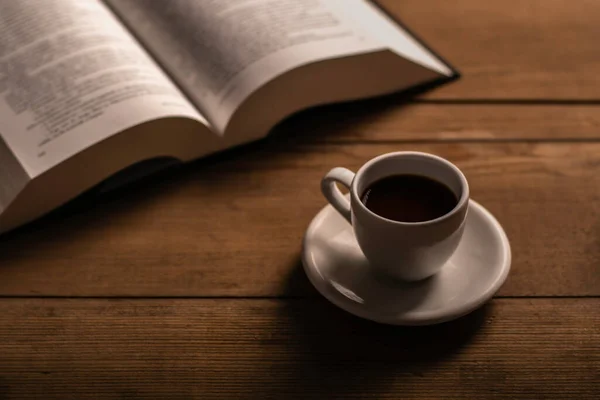 Kahverengi ahşap masada açık kitaplı bir fincan kahve.
