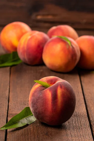 Fresh juicy peaches with leaves on brown wooden background.
