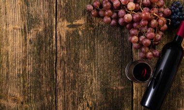 Ahşap bir masada üzümlü bir şişe kırmızı şarap. Kopyalama alanı olan üst görünüm.