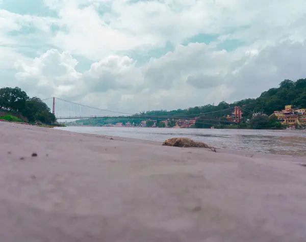 Rishikesh şehrinde Lakshman Jhulla yakınlarındaki kum plajı ve Ganj Nehri 'ni geçmek için köprü.