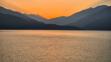 Peaceful pre-sunrise view at Tehri Lake in Uttarakhand, India. The calm water reflects the golden-orange glow of dawn while mountain silhouettes create a tranquil and scenic atmosphere. 