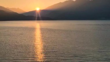 Beautiful 4K stock video of a sunrise over a calm lake with golden sun rays falling in a straight line across the water surface. Perfect for travel films, cinematic backgrounds, nature documentaries, meditation visuals, tourism projects.