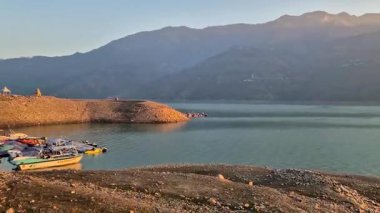 Stunning 4K stock video of sunrise over Tehri Lake in Uttarakhand, India. The golden sun rises behind the mountains with calm water reflections, creating a peaceful and scenic atmosphere. .