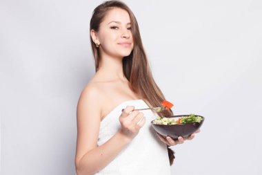 Güzellik, Cilt Bakımı ve insanlar kavramı - taze salata yemek ve gülümseyen havlu güzel esmer kız. Kadın yemek yeme. Akşam yemeği için taze sebze mutfakta sahip güzel gülümseyen kadın.