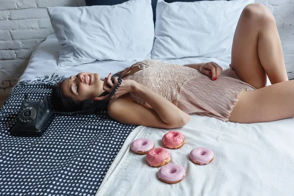 insanlar, tatlılar ve fast food kavramı - mutlu genç kadın veya genç kız çörek, yeme yatakta diz çökmüş. Güzel ince seksi kız tatlı çörek, Kahvaltı zamanı, Günaydın kavramı ile yatakta yatıyor