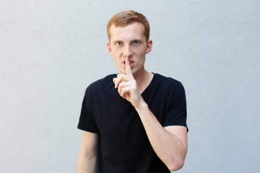 Moda, stil, duygular ve insanlar kavramı - Kızıl çilli bir gri ile güzel bir erkekçe adamın portresi yakından arka plan siyah T-shirt. dudaklarında parmak tutan dinleme cihazı gözlü erkek