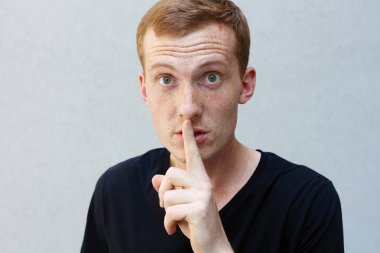 Moda, stil, duygular ve insanlar kavramı - Kızıl çilli bir gri ile güzel bir erkekçe adamın portresi yakından arka plan siyah T-shirt. dudaklarında parmak tutan dinleme cihazı gözlü erkek