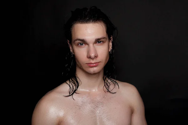 people, skincare and beauty concept - Wet young man with long black hair on a black background. Portrait male with shaved chest . Men\'s skin care. Ripped muscular handsome man on black background