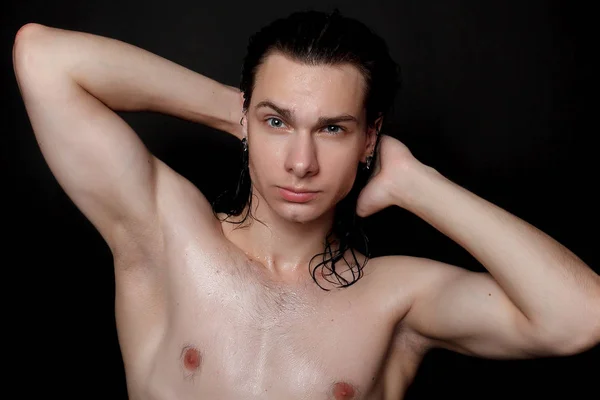 people, skincare and beauty concept - Wet young man with long black hair on a black background. Portrait male with shaved chest . Men\'s skin care. Ripped muscular handsome man on black background