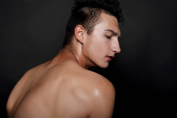 people, skincare and beauty concept - Wet young man with black hair on a black background. Portrait male with shaved chest . Men\'s skin care. Ripped muscular handsome man on black background