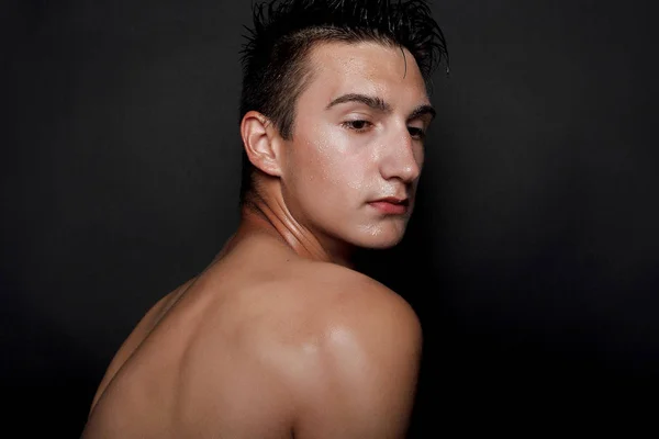 people, skincare and beauty concept - Wet young man with black hair on a black background. Portrait male with shaved chest . Men\'s skin care. Ripped muscular handsome man on black background