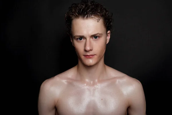 people, skincare and beauty concept - Wet young man with black hair on a black background. Portrait male with shaved chest . Men\'s skin care. Ripped muscular handsome man on black background