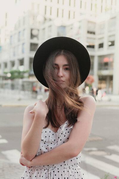 young teenage girl in a white dress and hat. style of the big city. Sunset sky and rays of the sun. Natural beauty pretty woman in black fedora hipster hat, on warm summer evening sunset in big city
