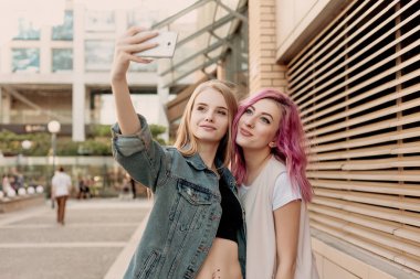 Bir akıllı telefon ile selfie alarak ve yüzleri ve eğlenceli hale arkadaşlar. Komik surat ve selfie için gülümseyen kız closeup. Fotoğrafta onların smartphone ile şehirde iki mutlu kız arkadaşım