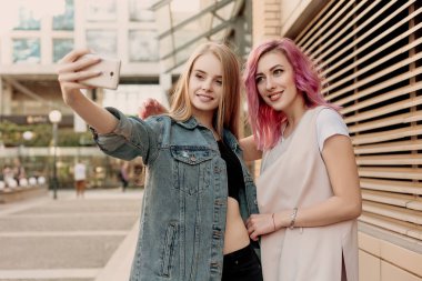 Bir akıllı telefon ile selfie alarak ve yüzleri ve eğlenceli hale arkadaşlar. Komik surat ve selfie için gülümseyen kız closeup. Fotoğrafta onların smartphone ile şehirde iki mutlu kız arkadaşım
