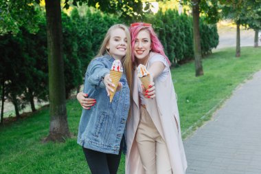 Şehirde takılmak süre kucaklayan hipster Genç Yetişkin arkadaşlar. İki genç kadın gülüyor ve kaygısız tatil yaşam tarzı zevk yürüme. İki güzel kız arkadaşım şehirde dondurma yeme