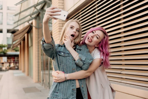 Friends taking selfie with a smart phone and making faces and fun. Closeup of girls making funny faces and smiling for selfie. Two happy girlfriends taking photo with their smartphone in the city
