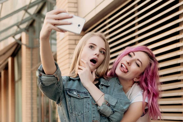 Friends taking selfie with a smart phone and making faces and fun. Closeup of girls making funny faces and smiling for selfie. Two happy girlfriends taking photo with their smartphone in the city