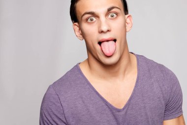 duygu, reklam ve insanlar kavramı - yakışıklı genç adam kameraya bakarak gri arka plan üzerinde. Seksi bir adam portresi. Mutlu adam gülümsüyor. Genç adam dilini gösterir