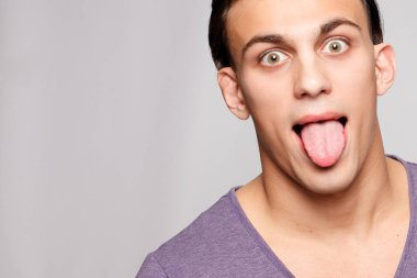 duygu, reklam ve insanlar kavramı - yakışıklı genç adam kameraya bakarak gri arka plan üzerinde. Seksi bir adam portresi. Mutlu adam gülümsüyor. Genç adam dilini gösterir