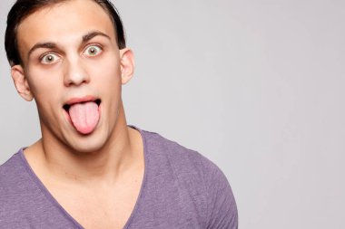 duygu, reklam ve insanlar kavramı - yakışıklı genç adam kameraya bakarak gri arka plan üzerinde. Seksi bir adam portresi. Mutlu adam gülümsüyor. Genç adam dilini gösterir
