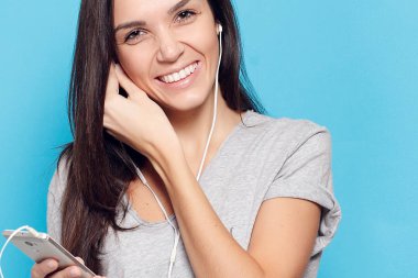 teknoloji, yaşam tarzı, internet bağımlılığı ve insanlar kavramı - akıllı telefon olan güzel kadın. mavi bir arka plan üzerinde kulaklık ile neşeli bir kadın. Mutlu ve gülümseyerek çekici kadın