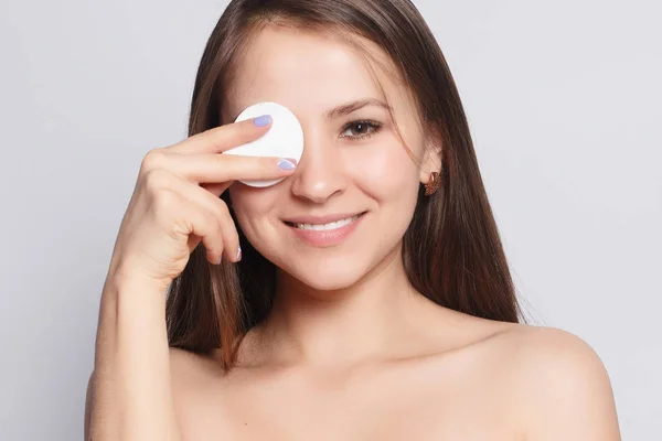 Woman using cotton pad. Happy smiling beautiful young woman cleaning skin by cotton pad. light background. Beautiful Spa Woman Smiling. Perfect Fresh Skin. Youth and Skin Care Concept