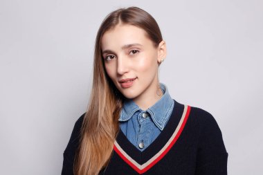 Güzel, neşeli bir kadın, sarışın, sıradan giyinmiş, kameraya tatmin edici bir şekilde bakıyor, mutlu. Güzel bir kadının stüdyo resmi. Boş bir stüdyo duvarında izole edilmiş..