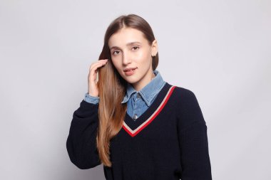 Güzel, neşeli bir kadın, sarışın, sıradan giyinmiş, kameraya tatmin edici bir şekilde bakıyor, mutlu. Güzel bir kadının stüdyo resmi. Boş bir stüdyo duvarında izole edilmiş..
