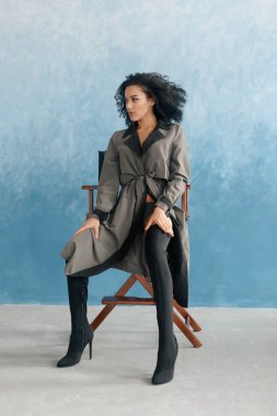 insanlar, ırk, etnik köken ve moda kavramı - güzellik siyah model çizmeler içinde poz. Film, yönetmen 's sandalyede oturan genç güzel güzel melez kadın. gri yağmurluk, afro saç kadında