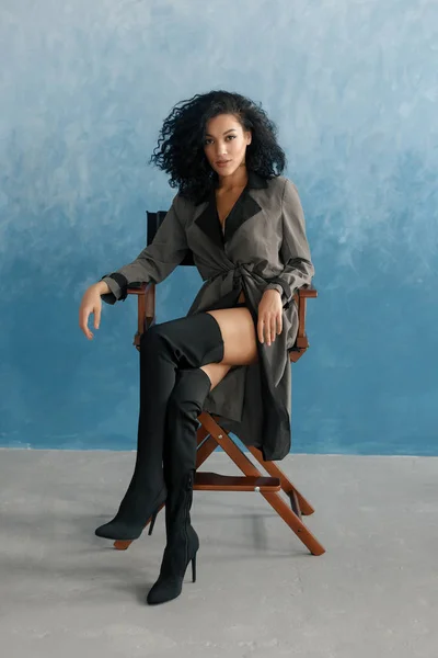 种族和时尚概念 美丽的黑色模型摆在高靴 年轻漂亮的黑白混血女人坐在导演的椅子上电影 穿灰色雨衣的女人 黑人发型 — 图库照片