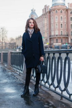 Hevesli gülümseyen kız ile parlak güneş ışığı altında şehirde poz bukleler. Yakın çekim açık harika gülümseme ve büyük mavi gözleri ile moda sonbahar siperde büyüleyici Bayan portresi.