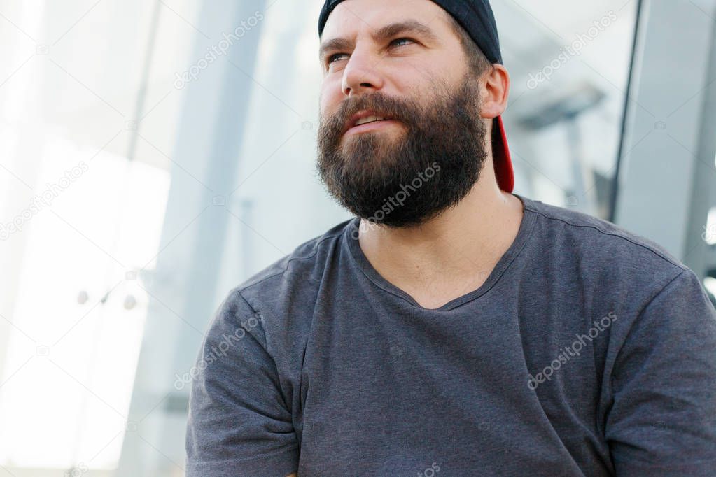 Closeup of smiling young man looking at camera. Portrait of a guy with beard who changes facial expressions. Proud and satisfied man with t-shirt looking at camera.