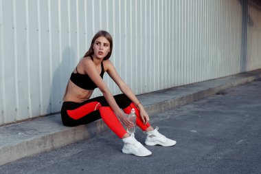Kadın atlet içme suyu gri bir duvar tarafından dururken. İnce kadın egzersiz yaptıktan sonra bir mola spor giyim.