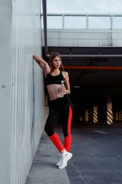 Kadın atlet içme suyu gri bir duvar tarafından dururken. İnce kadın egzersiz yaptıktan sonra bir mola spor giyim.