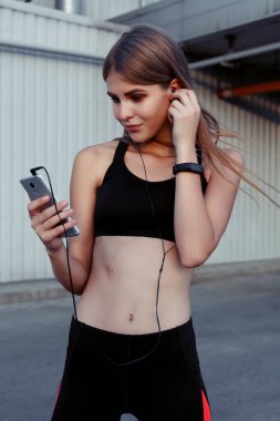 Kadın atlet dinlenme çalışmadan sonra şehirde alarak. Müzik ve gülerek seyir kulaklıklar ile spor Fitness kadında.