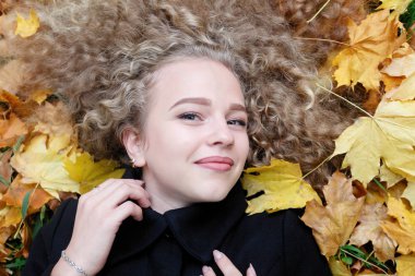 Kıvırcık saçlı, yeşil gözlü güzel genç kadın. giysili kızı rahat rahatlatıcı parkta güzel bir sonbahar havası, düşen yapraklar ile kaplı.