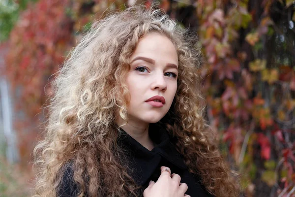 Beautiful young woman with curly hair, green eyes. girl in casual clothes relaxing in park in good autumn weather, covered with fallen leaves.