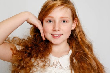 Çok güzel bir kırmızı saçlı kız gri bir arka plan üzerinde eğlenceli portresi. Güzellik, çocuk moda, kozmetik, sağlıklı saçlar. Kuaför, makyaj, şampuan.