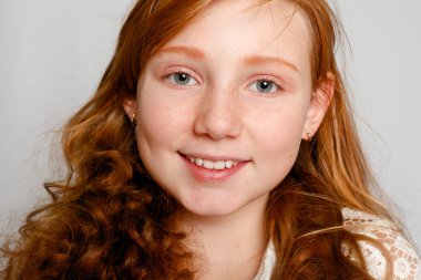 Çok güzel bir kırmızı saçlı kız gri bir arka plan üzerinde eğlenceli portresi. Güzellik, çocuk moda, kozmetik, sağlıklı saçlar. Kuaför, makyaj, şampuan.