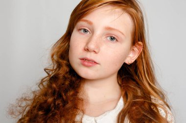 Çok güzel bir kırmızı saçlı kız gri bir arka plan üzerinde eğlenceli portresi. Güzellik, çocuk moda, kozmetik, sağlıklı saçlar. Kuaför, makyaj, şampuan.