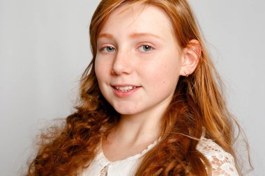 Çok güzel bir kırmızı saçlı kız gri bir arka plan üzerinde eğlenceli portresi. Güzellik, çocuk moda, kozmetik, sağlıklı saçlar. Kuaför, makyaj, şampuan.