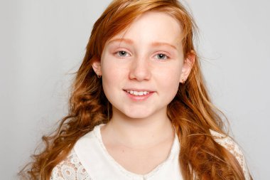 Çok güzel bir kırmızı saçlı kız gri bir arka plan üzerinde eğlenceli portresi. Güzellik, çocuk moda, kozmetik, sağlıklı saçlar. Kuaför, makyaj, şampuan.