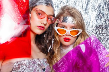 Gümüş arka plan üzerinde genç güzel iki kız arkadaşlar. Sanat fantezi makyaj sanatsal kadınla tarz. Vogue tarzı. Yaratıcılık. Moda kız. Güzellik kadın portre. Renk filtreleri ile güzellik yüz